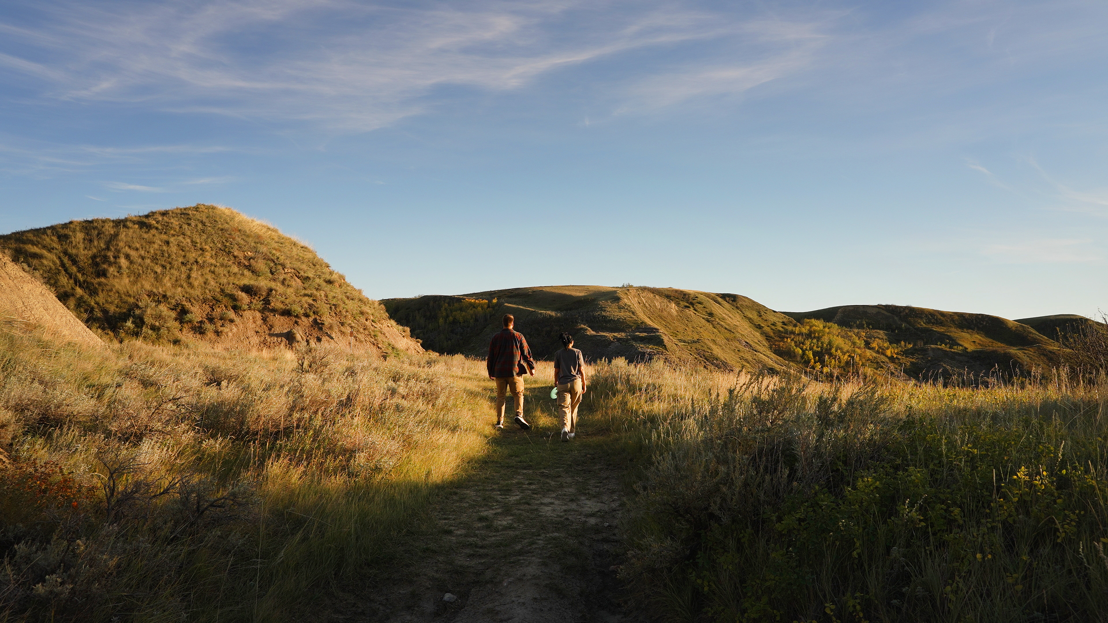 Hero Image - two people walking over grassy dunes